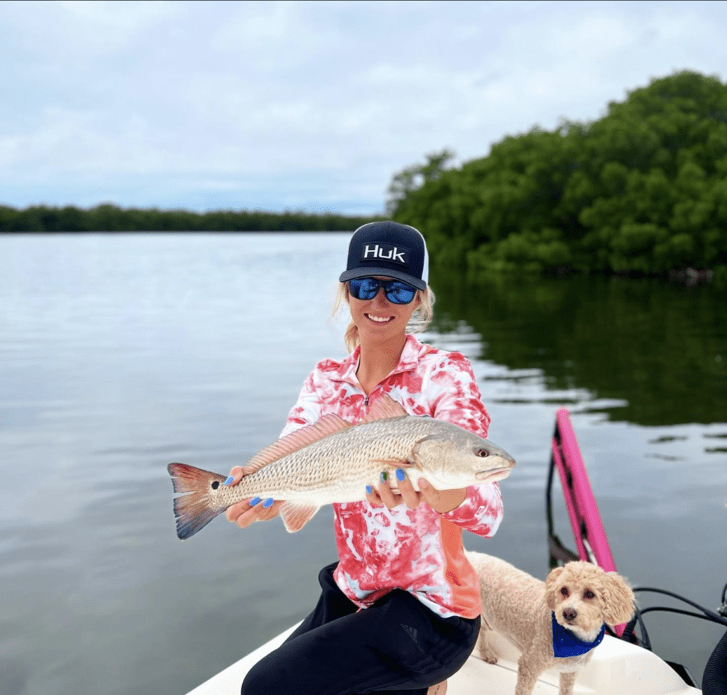 Chasten Whitfield smiling on boat holding fish with small dog next to her