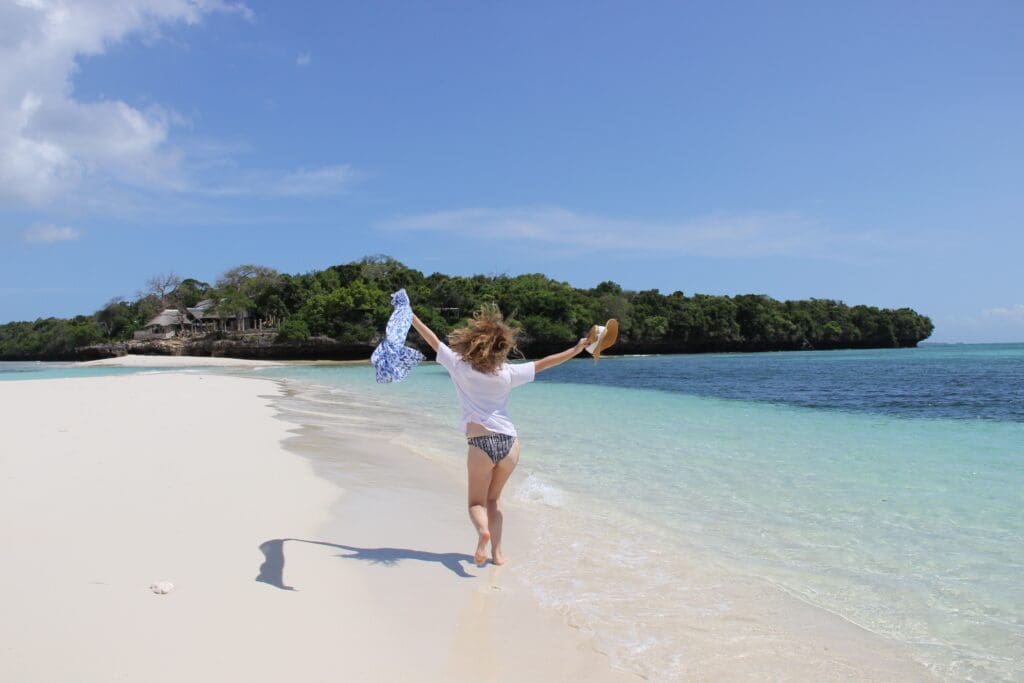 Woman running on white sand beach next to crystal blue water of Pemba Island, Africa