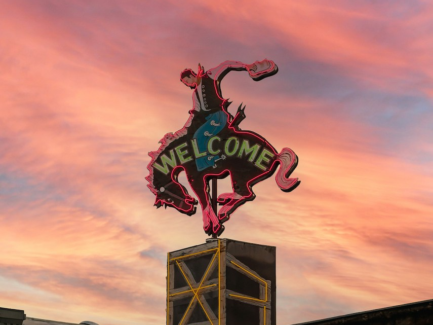Neon bucking horse sign in Wyoming that says "welcome" with pink sunset in background